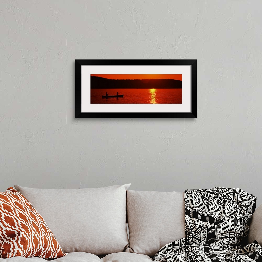 A bohemian room featuring This panoramic piece is a picture taken of two people canoeing on a lake during sunset which has ...
