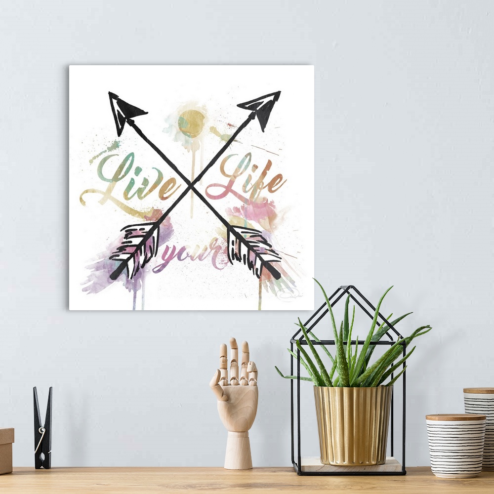 A bohemian room featuring "Live Your Life" watercolor painting with black crisscross arrows splitting up the words.