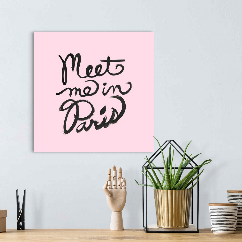A bohemian room featuring "Meet Me In Paris" hand lettered in black on a pastel pink background.
