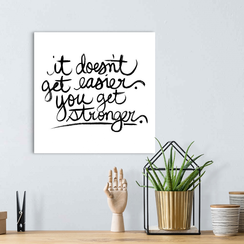 A bohemian room featuring Square decor with black handwritten text reading "it doesn't get easier. you get stronger" on a s...