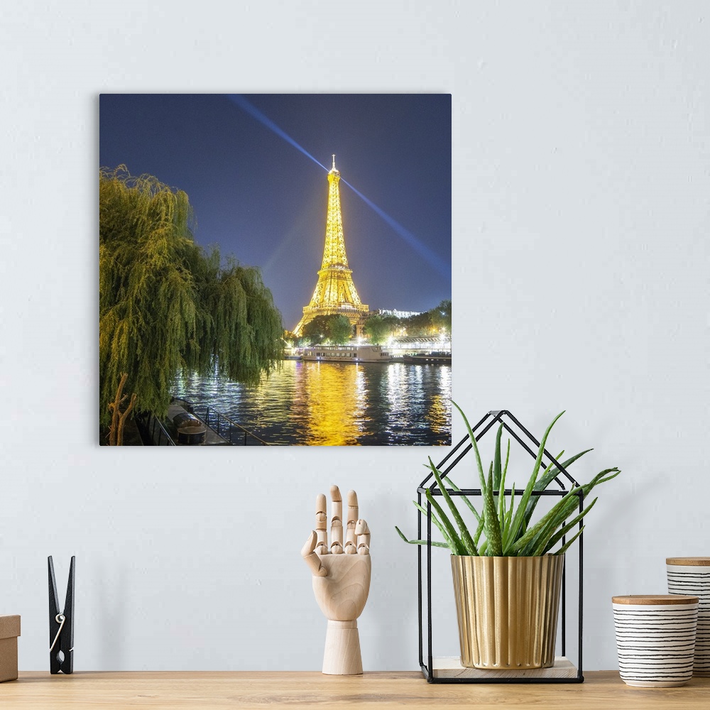 A bohemian room featuring National french monument Eiffel tower lighting at night with boat on the Seine river with trees o...