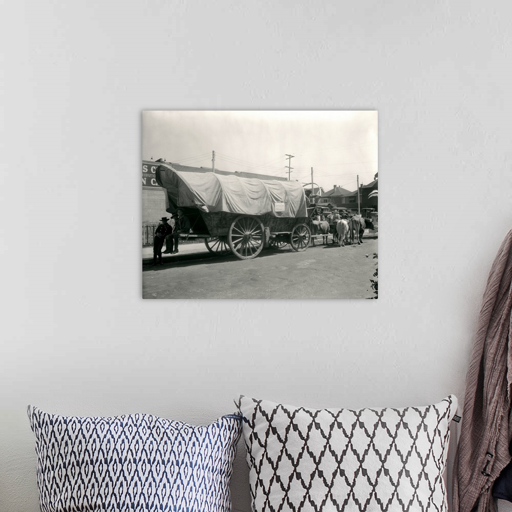 A bohemian room featuring 1920's Ox Drawn Conestoga Covered Wagon Parked Along Street.