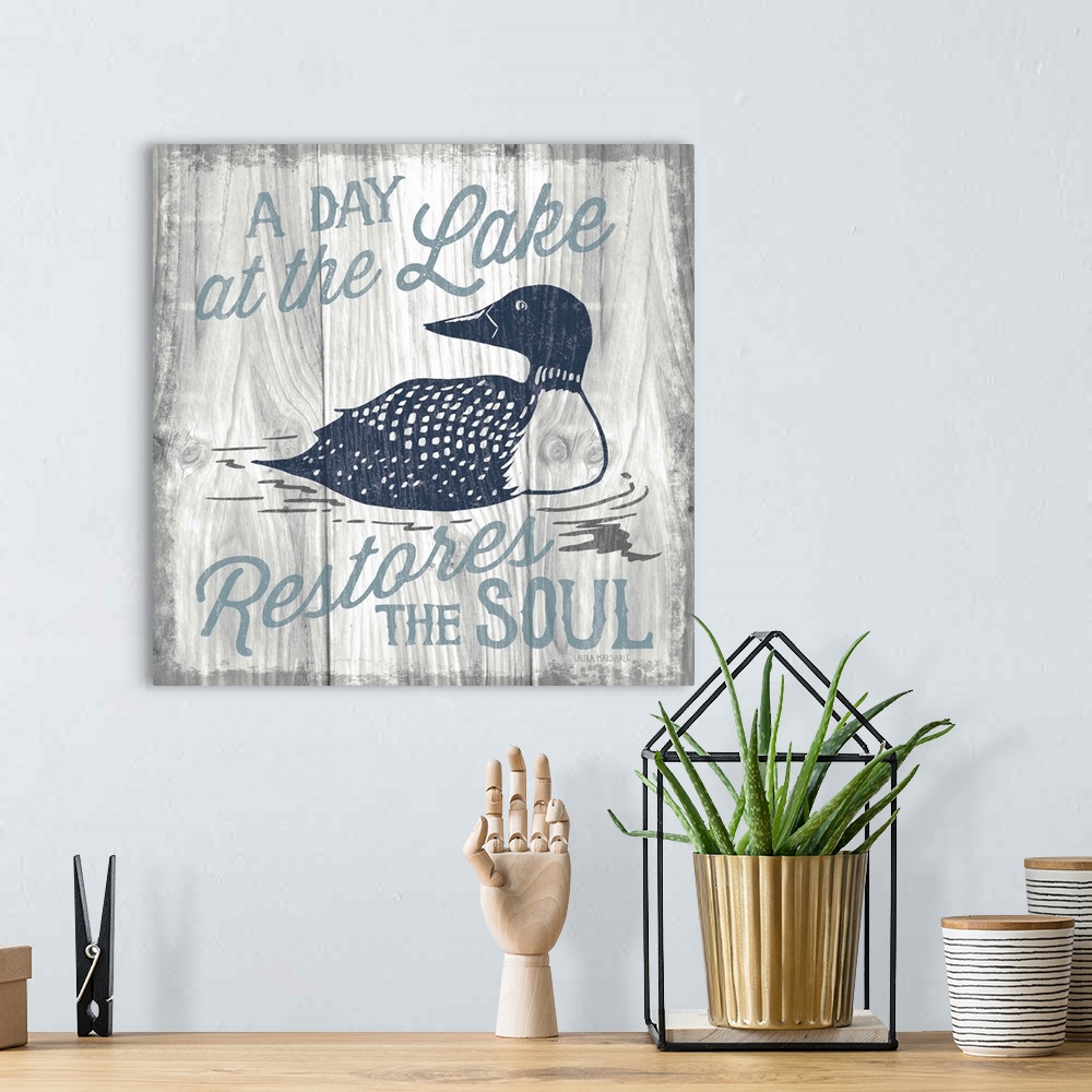 A bohemian room featuring "A Day at the Lake Restores the Soul" in blue with an illustration of a duck on a grey wood grain...