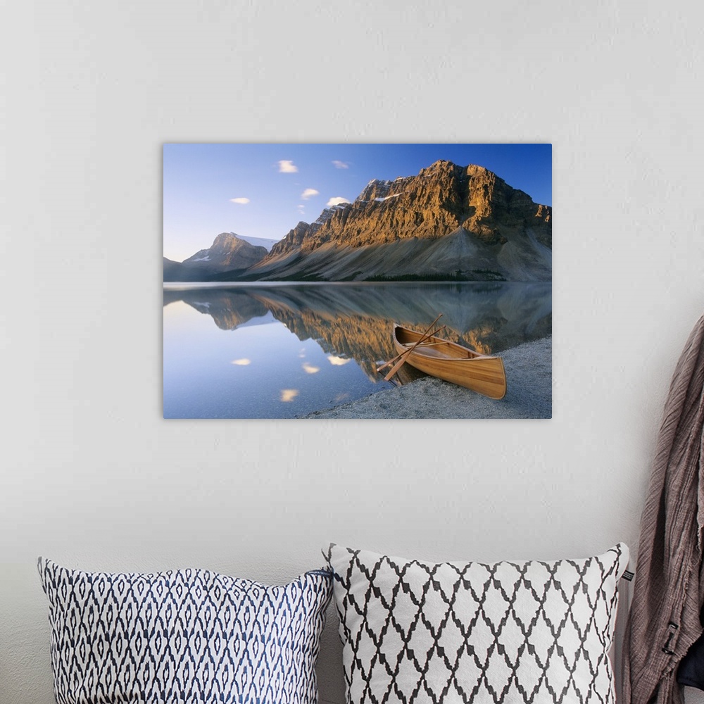 A bohemian room featuring Oversized photography artwork of a canoe sitting on the edge of water with mountains in the backg...