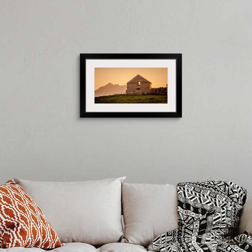 A bohemian room featuring Warm photograph of an old wooden barn on a hilltop with a silhouette of mountains in the background.