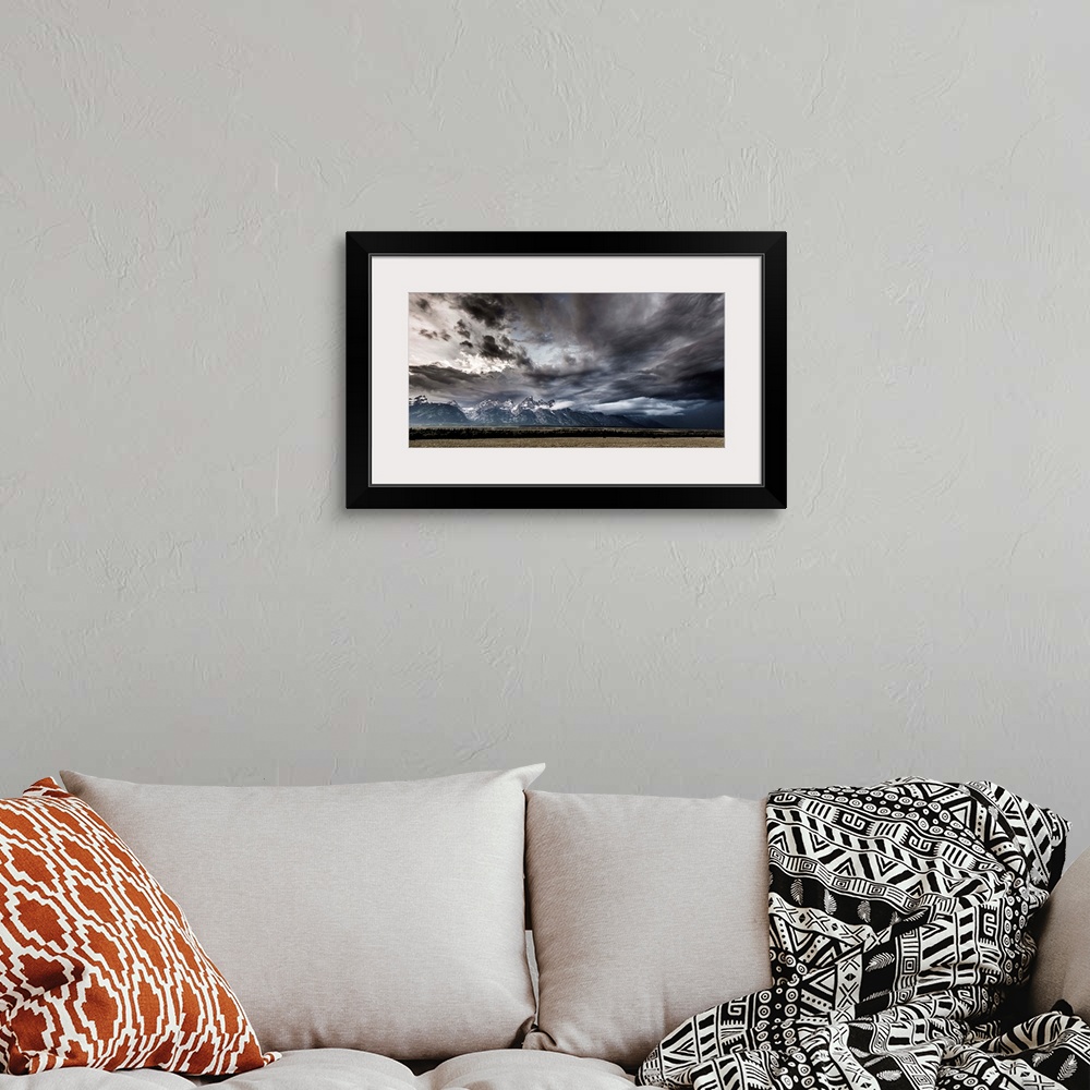 A bohemian room featuring Landscape photograph of a field in front of snow capped mountains with a dramatic stormy sky above.