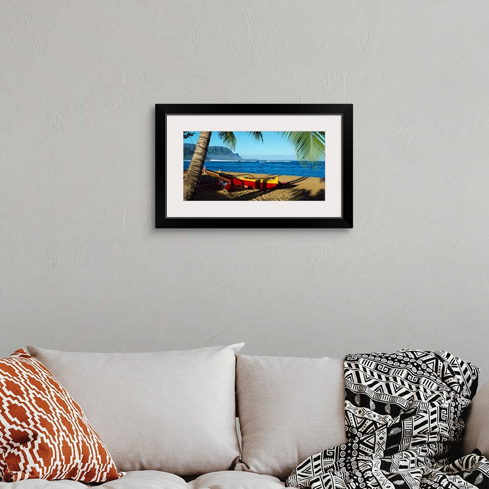 A bohemian room featuring Oversize wall art of a landscape photograph of a sailboat pulled up the shore and resting in the ...