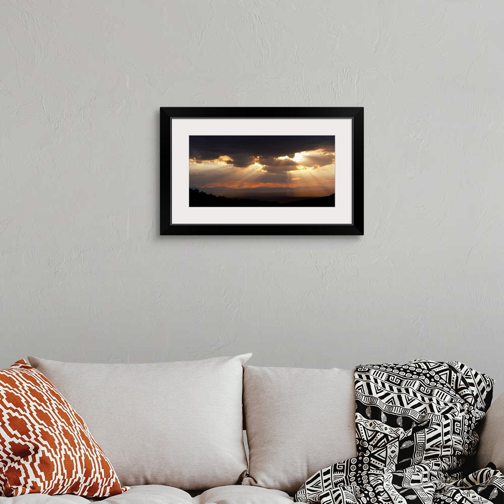 A bohemian room featuring Horizontal, large photograph of sunlight beaming through a sky full of huge, dark clouds, over th...
