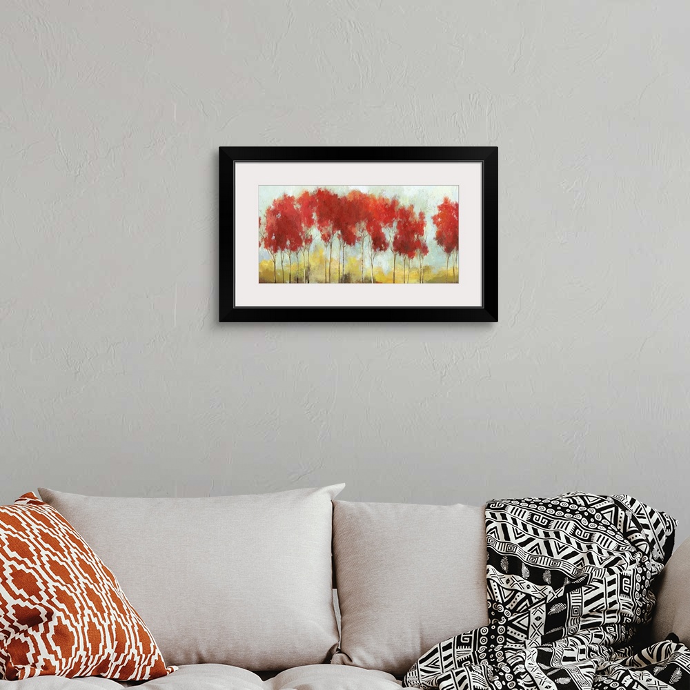 A bohemian room featuring A long horizontal painting of a row of trees with bright red leaves in the fall.