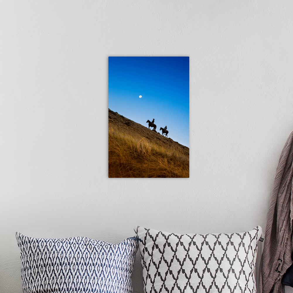 A bohemian room featuring Two wranglers riding horses up a hill with full moon in backround at blue hour