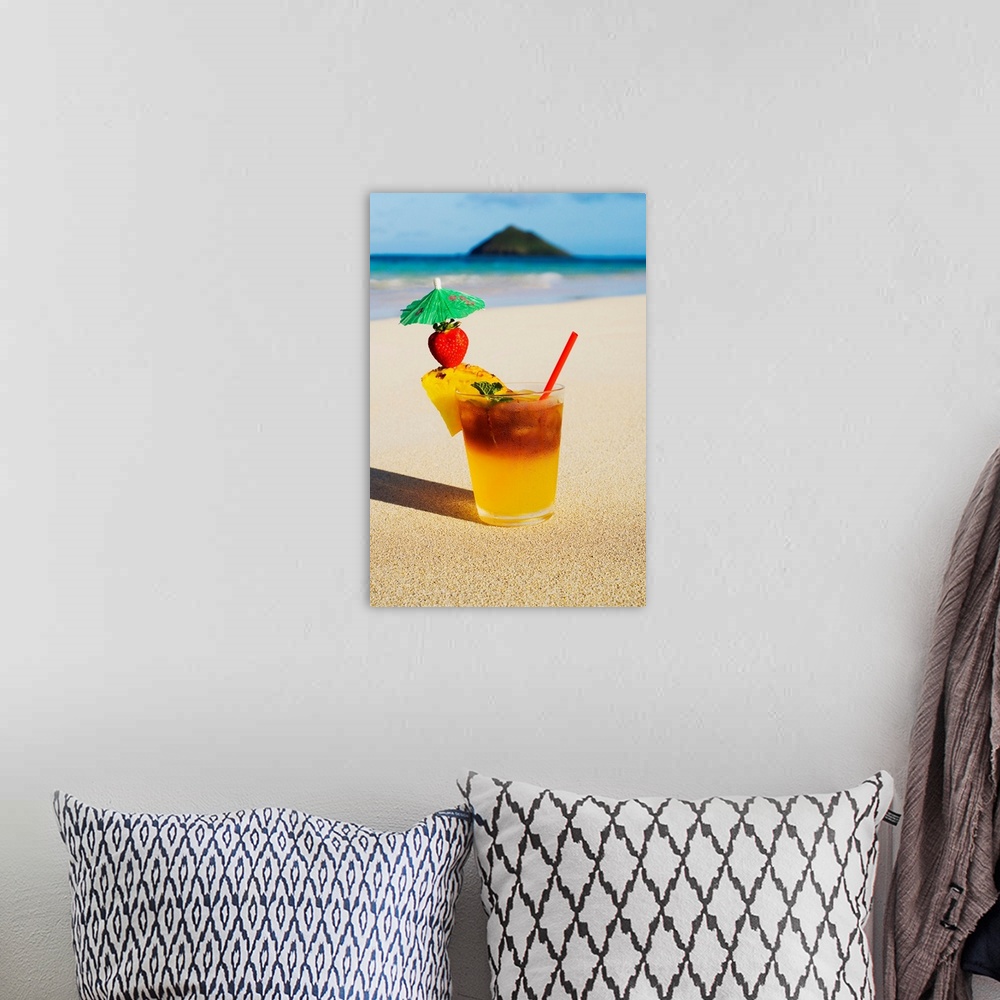A bohemian room featuring A mai tai garnished with pinapple and a strawberry, sitting in the sand on the beach.