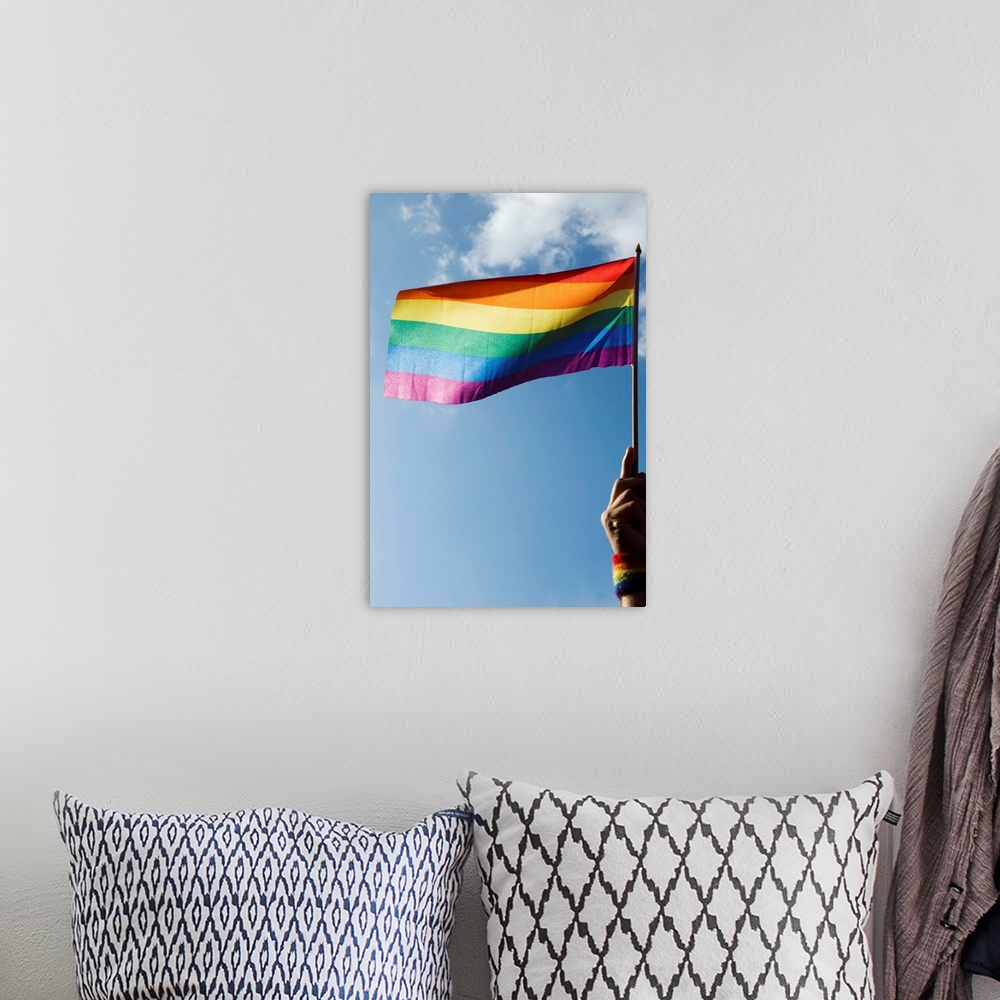 A bohemian room featuring Person's hand holding rainbow-colored flag waving in the sky