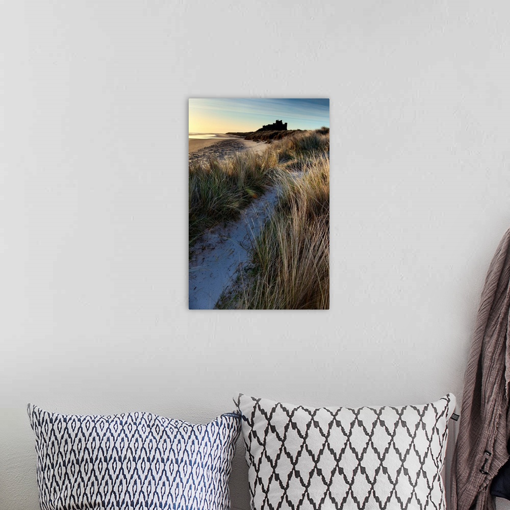 A bohemian room featuring Bamburgh Castle, Northumberland, UK lit by soft golden light with a blue sky over windsept marram...