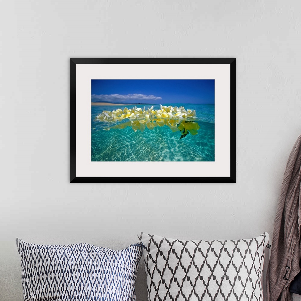 A bohemian room featuring Horizontal photograph on a large wall hanging of a lei of golden plumeria flowers, floating on cl...