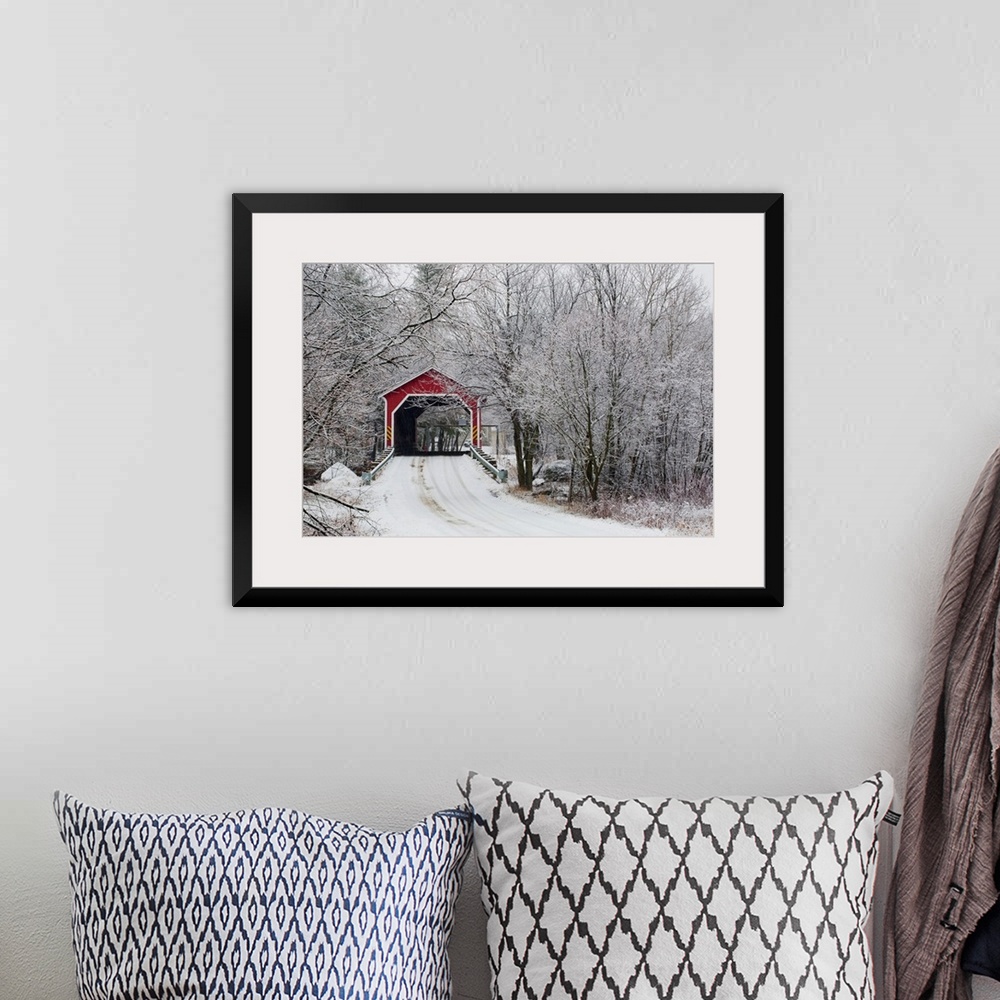 A bohemian room featuring Snow covered trees surround a road that leads up to a covered bridge.