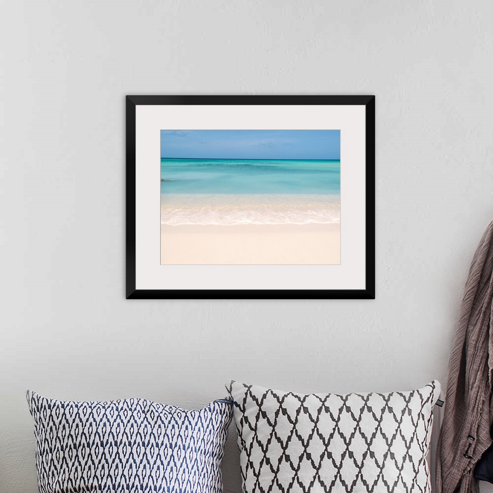 A bohemian room featuring Horiztonal wall art of a serene beach and a still sea on a clear day in Aruba.