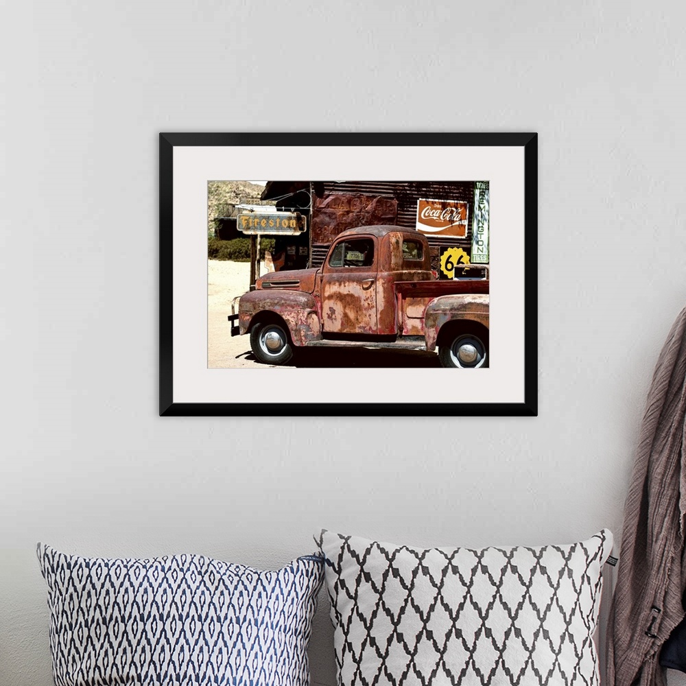 A bohemian room featuring A very rusty pickup truck sits by a weathered gas station on Route 66.