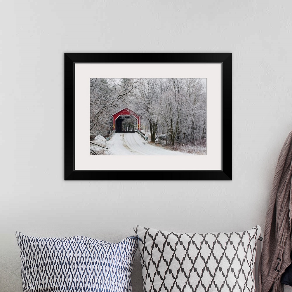 A bohemian room featuring Snow covered trees surround a road that leads up to a covered bridge.