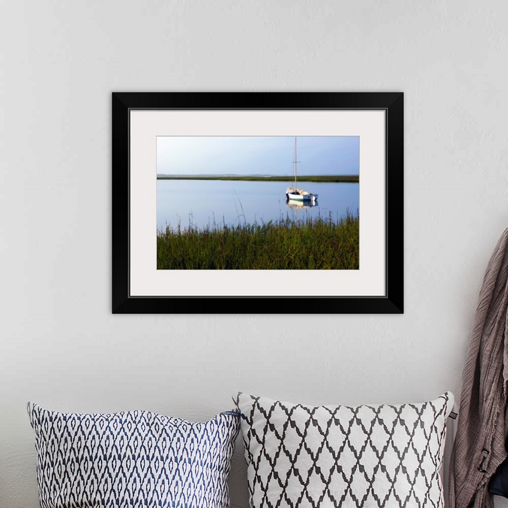 A bohemian room featuring A landscape photograph of a sailboat anchored in still waters surrounded by marshy grasses on the...