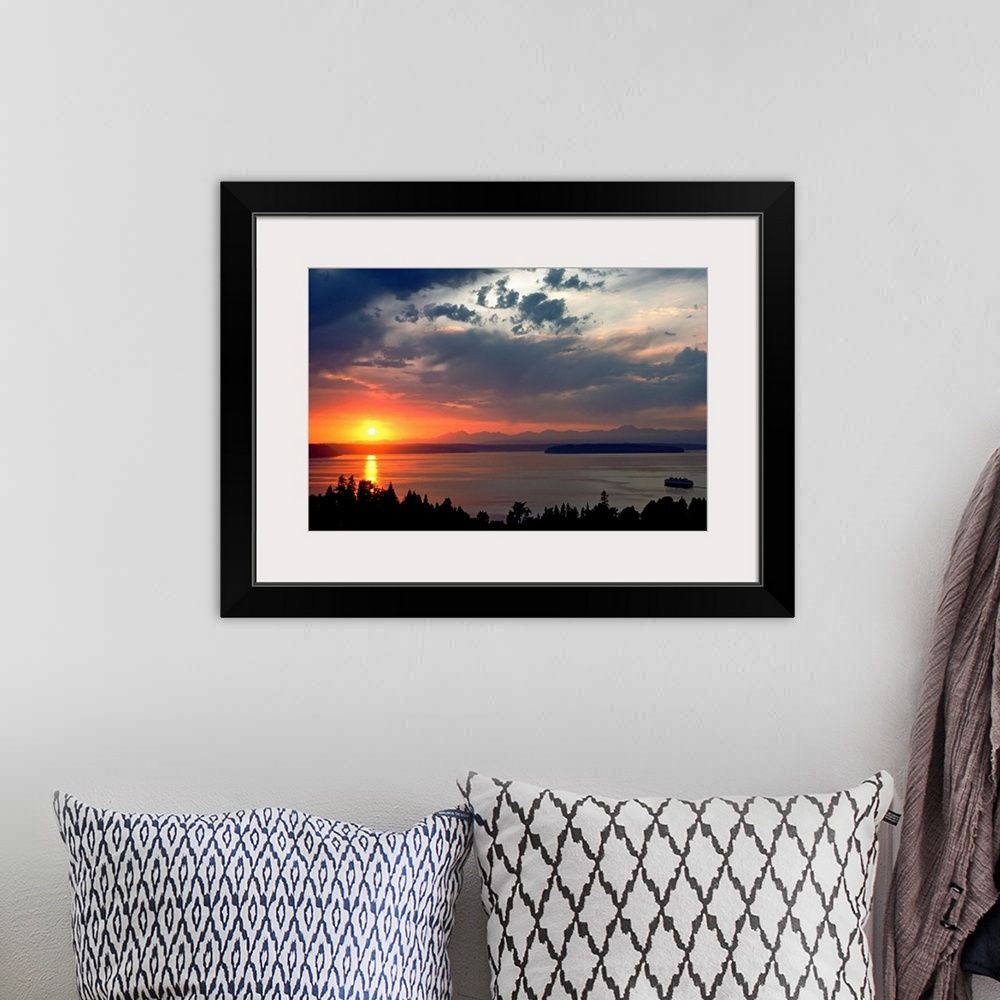 A bohemian room featuring Horizontal photograph of a vibrant setting sun in a partly cloudy sky, over a large body of water...