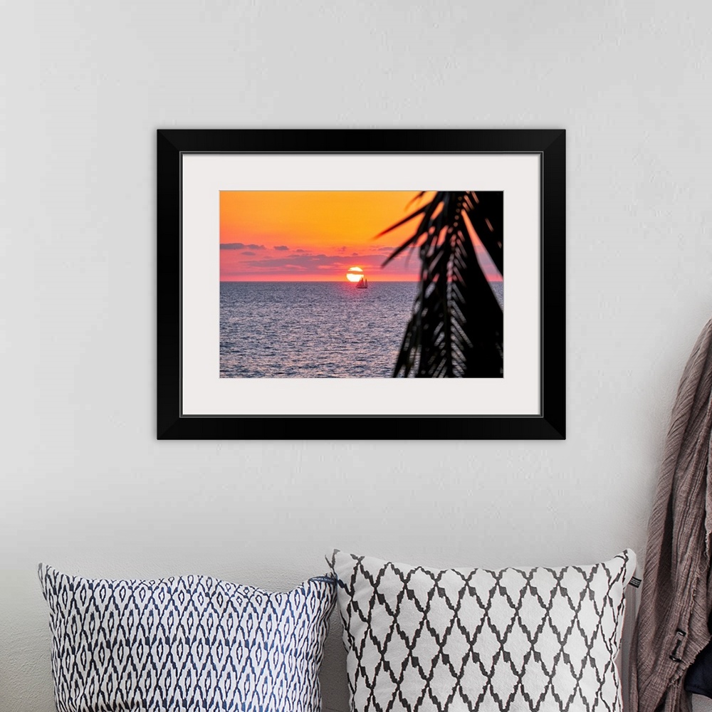 A bohemian room featuring A photo of sun setting behind a boat on water in Puerto Vallarta, Mexico with a palm tree leaf on...