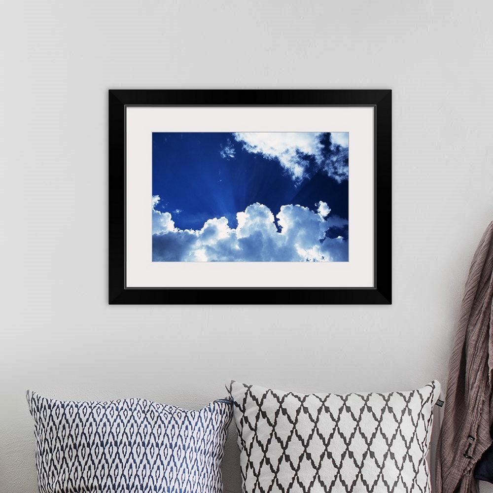 A bohemian room featuring Sunbeams behind billowing white clouds, blue sky.