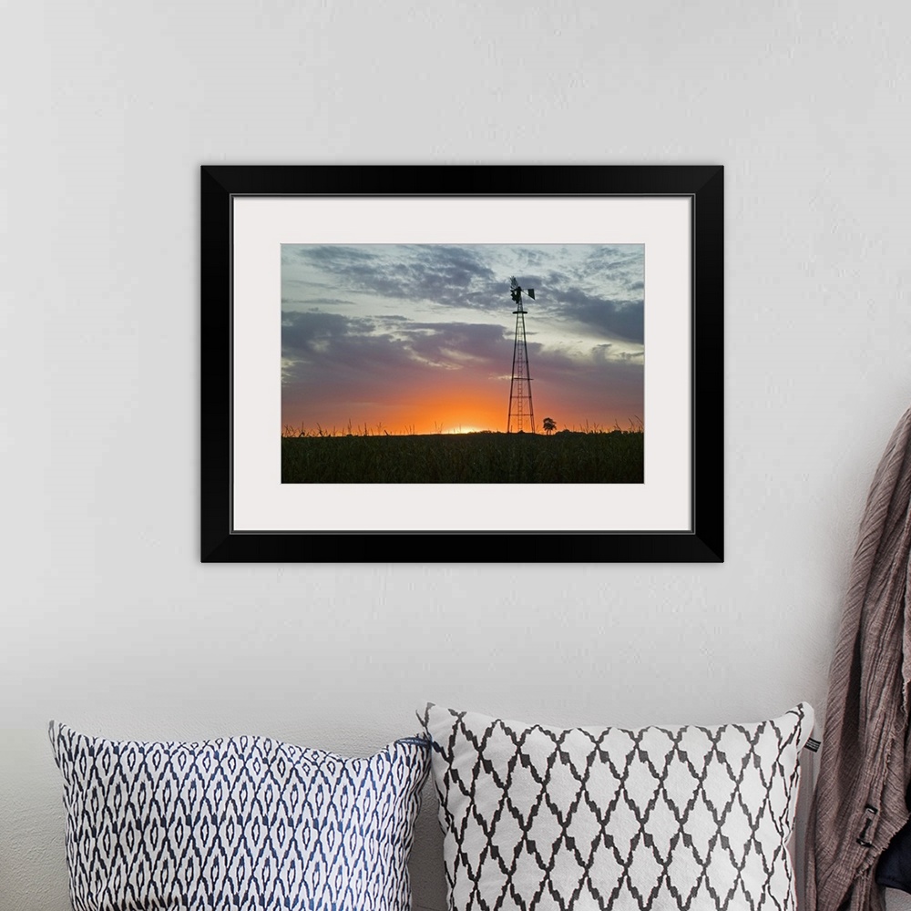 A bohemian room featuring A tall windmill rises above a crop field on a farm with just the edge of the setting sun peeking ...