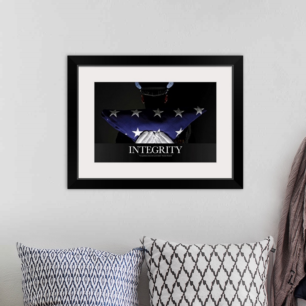 A bohemian room featuring A silhouette of a soldier is shown as he holds up a folded American flag. The word "Integrity" is...
