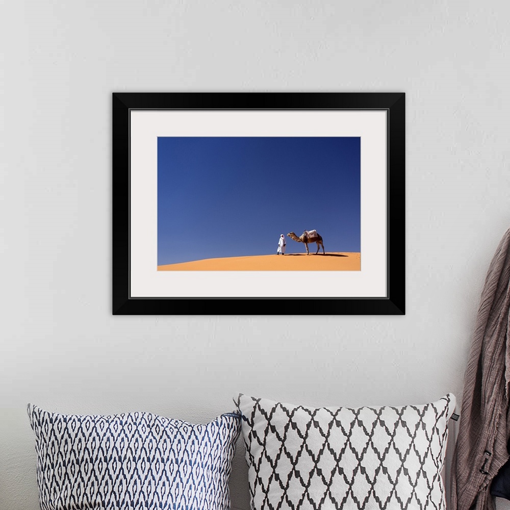 A bohemian room featuring Berber man with camel on the ridge of an orange sand dune in the Erg Chebbi sand sea, Sahara Dese...