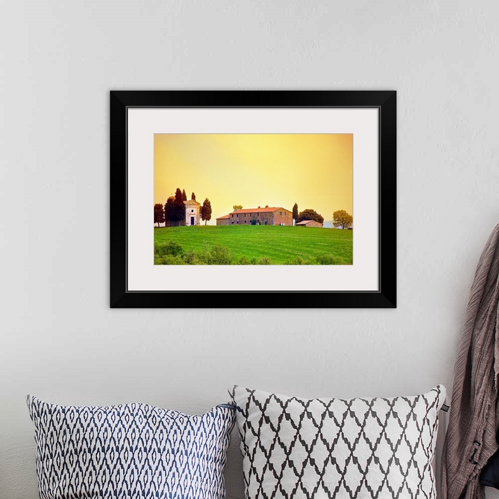 A bohemian room featuring Old traditional Tuscan farm buildings set on a green grass hill with a clear sunset sky.