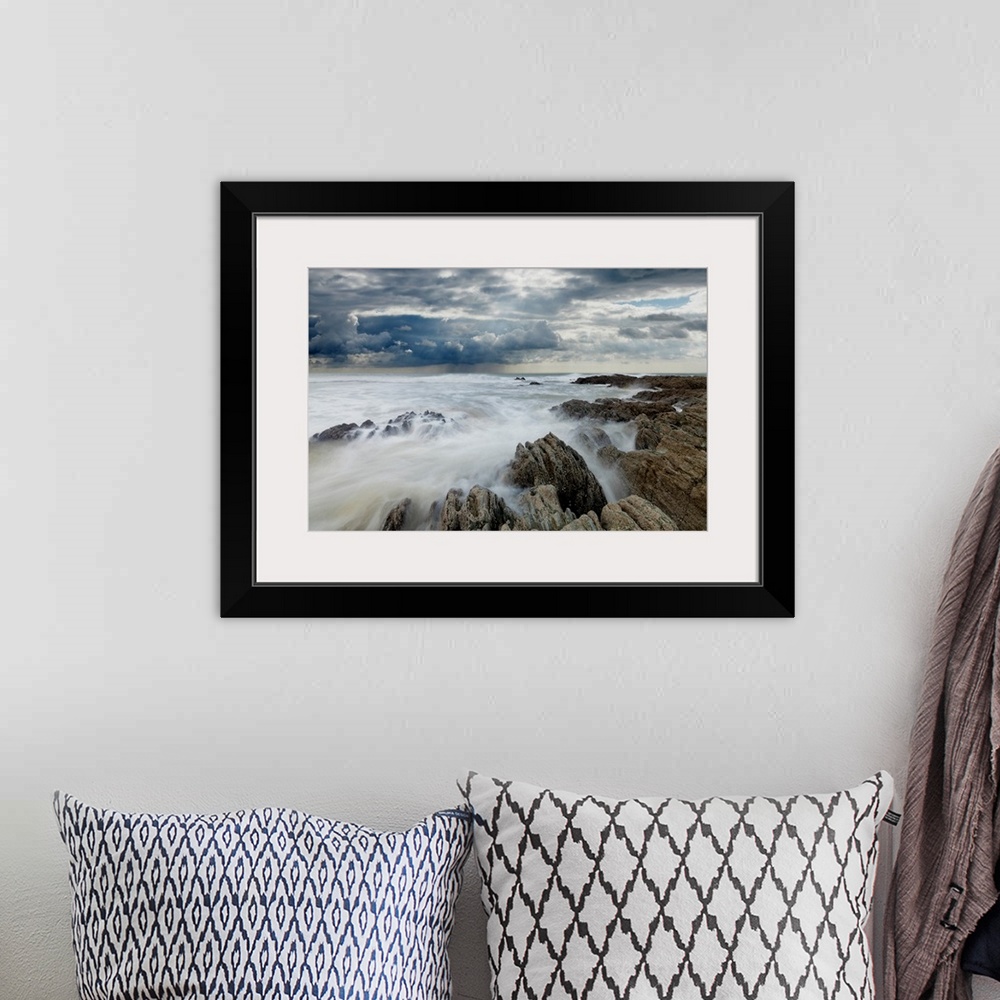 A bohemian room featuring Jagged rocks on coastline with white surf under grey storm clouds