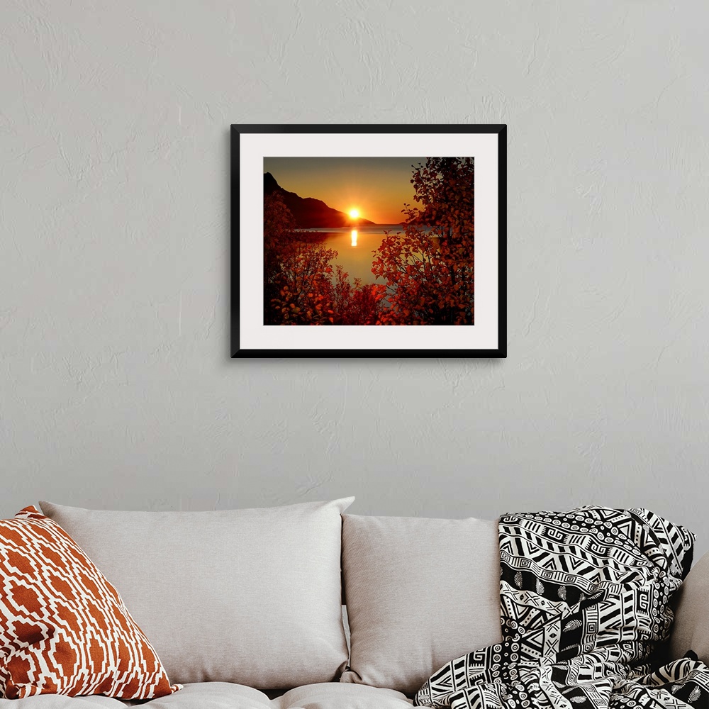 A bohemian room featuring Big photograph emphasizes the sun as it begins to set over a mountain and then reflect over a cal...