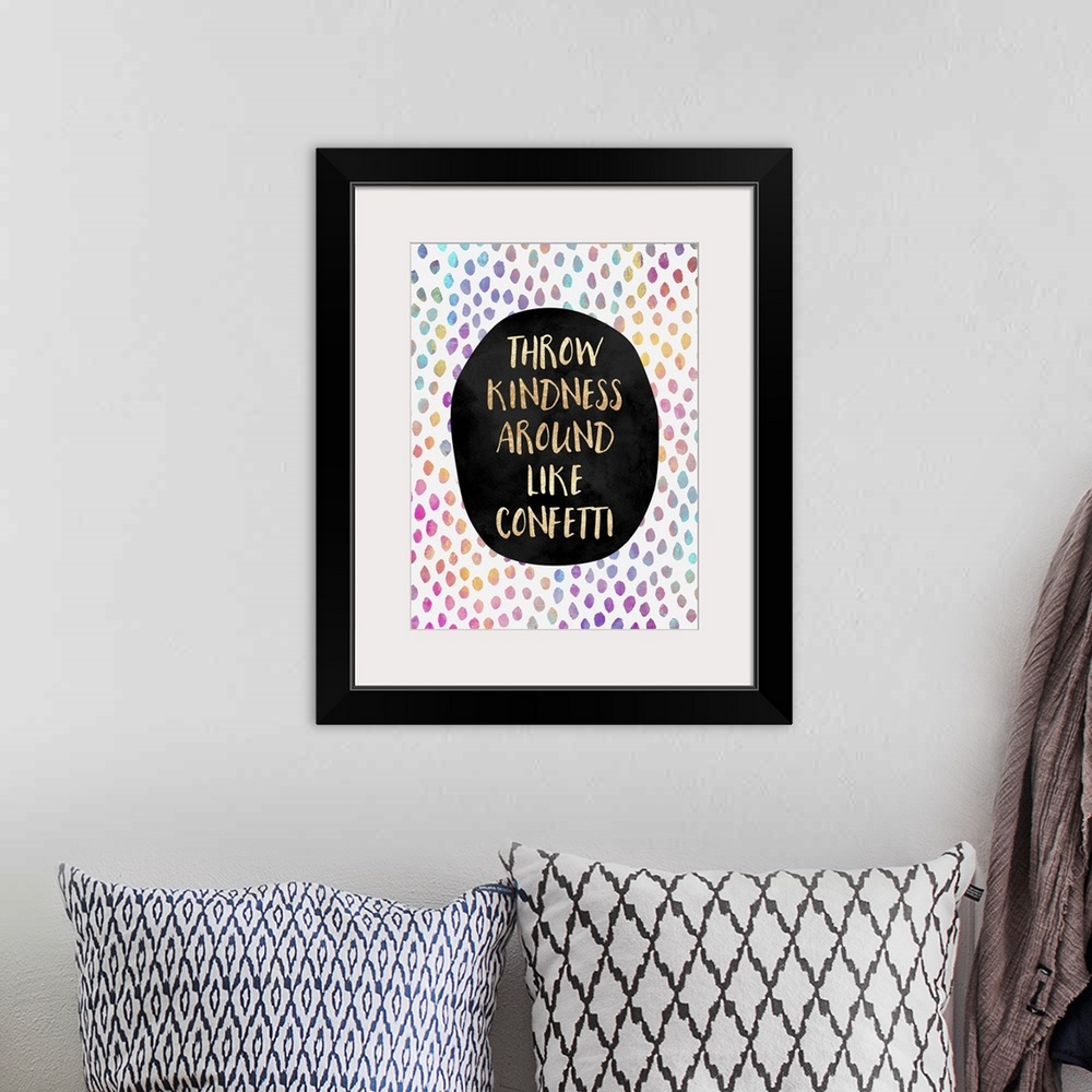 A bohemian room featuring The words 'throw kindness around like confetti' in gold letters on a black oval, surrounded by ra...