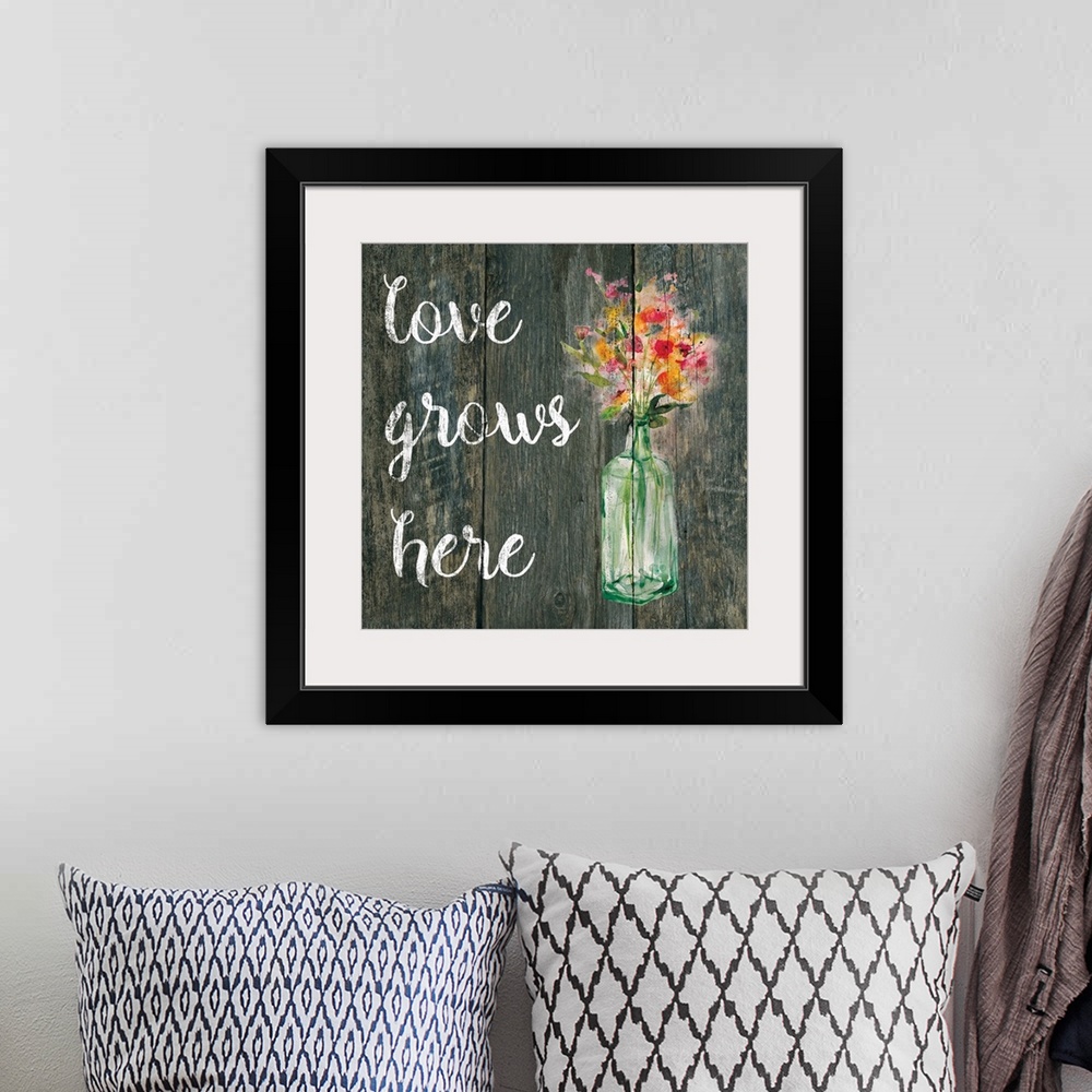 A bohemian room featuring "Love Grows Here" written in white on a faux wood background with pink and orange flowers in a gl...