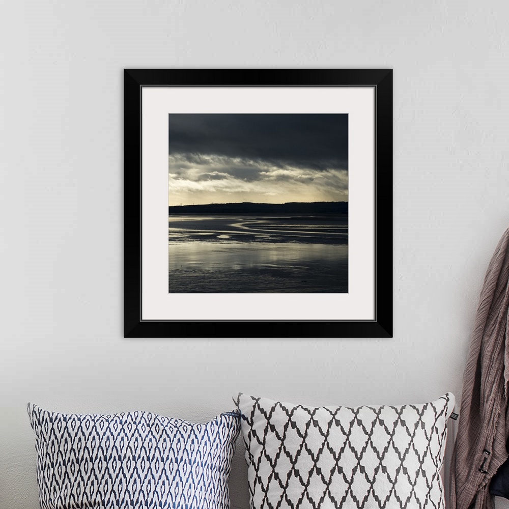 A bohemian room featuring A photograph of a watery landscape under dark clouds.