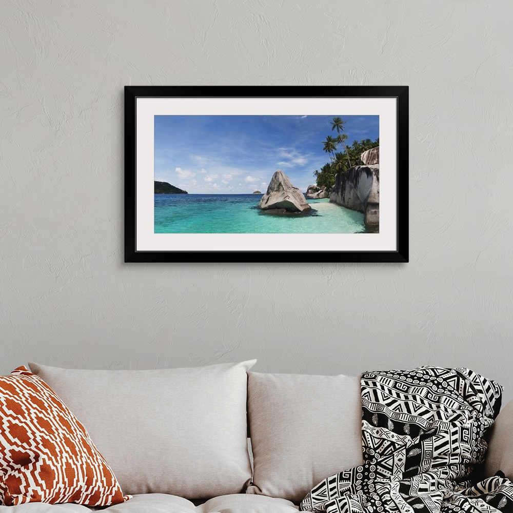 A bohemian room featuring Landscape photograph on a large canvas of clear blue waters in Malaysia, along the rocky shorelin...