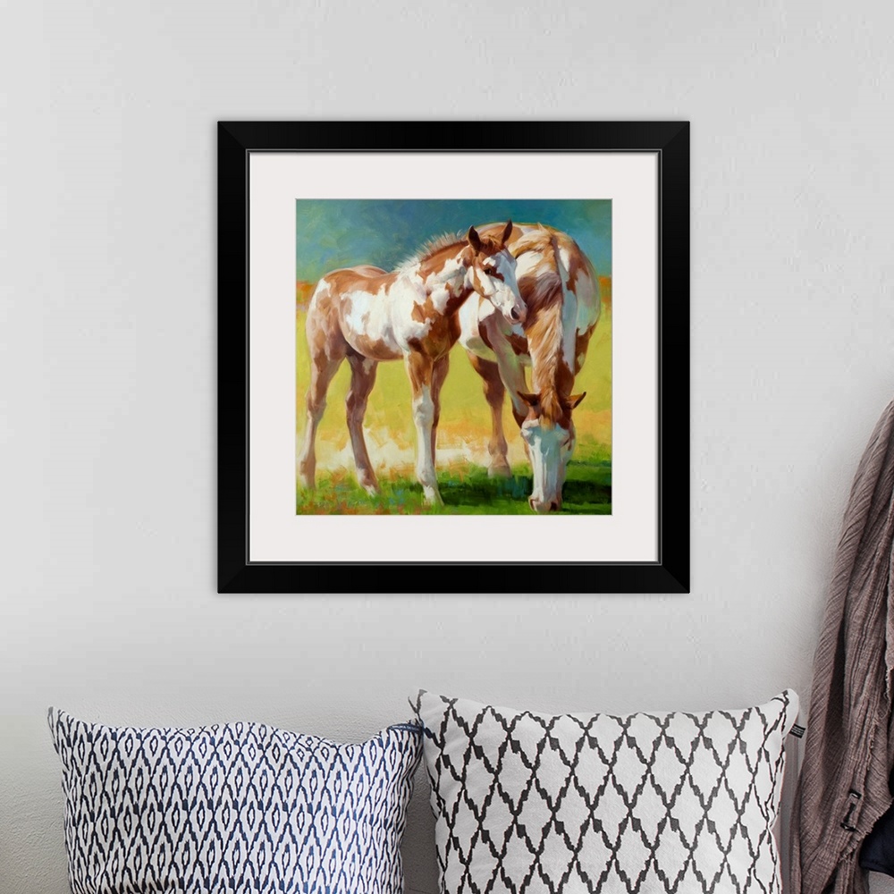 A bohemian room featuring A Paint mare and her foal grazing in a field in soft light.
