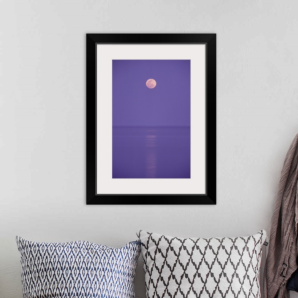 A bohemian room featuring a pink full moon hangs centered over a still body of water in the purple night