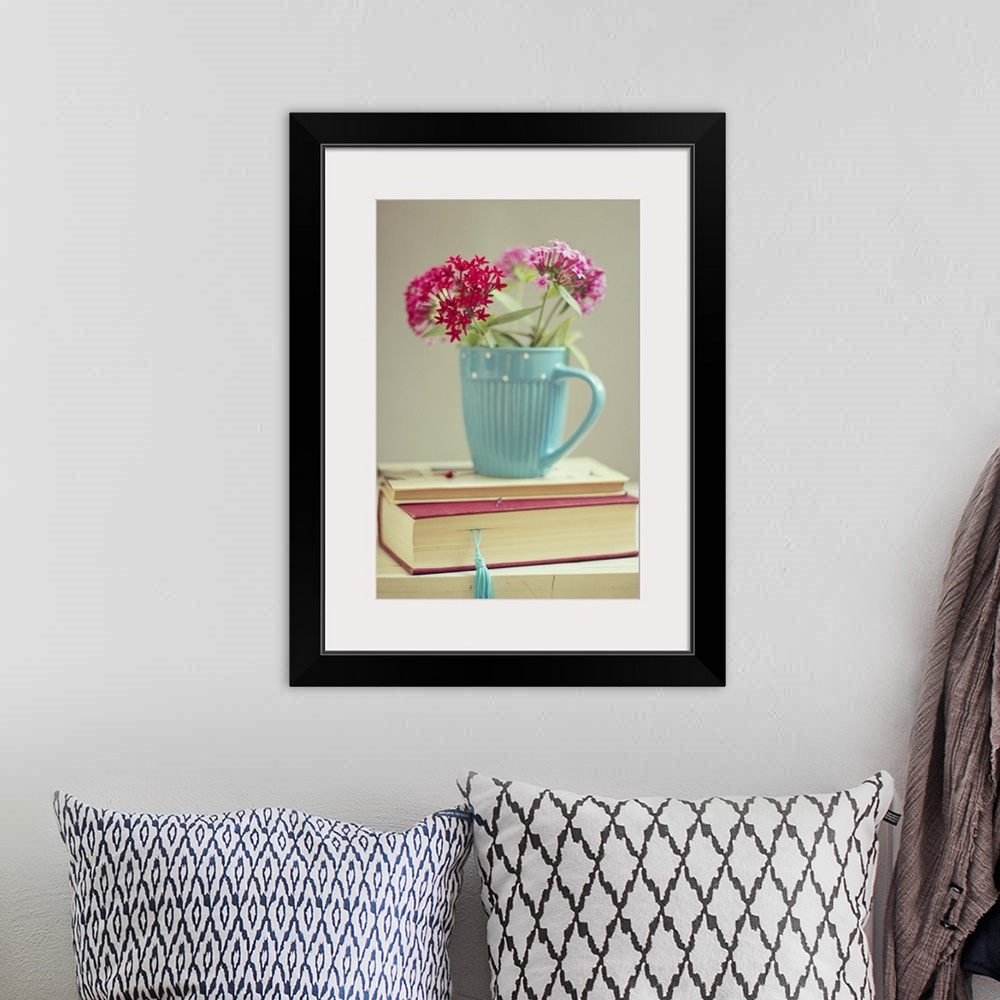 A bohemian room featuring Flowers in blue cup on two books.
