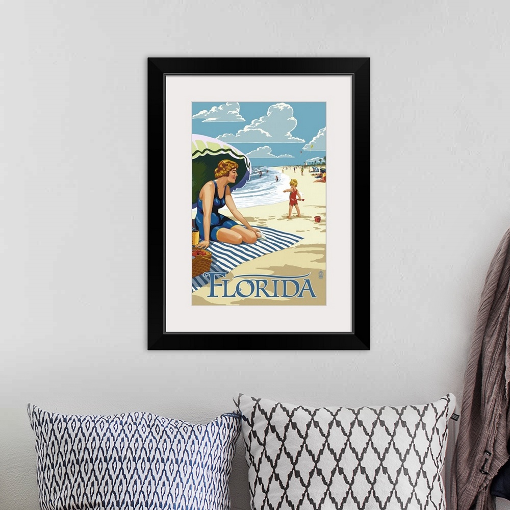 A bohemian room featuring Retro stylized art poster of a beach scene, with a woman sitting on a blanket under a an umbrella.