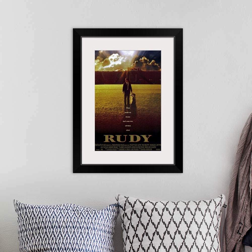 A bohemian room featuring This large vertical piece is a movie poster for "Rudy". It pictures the star character walking ac...