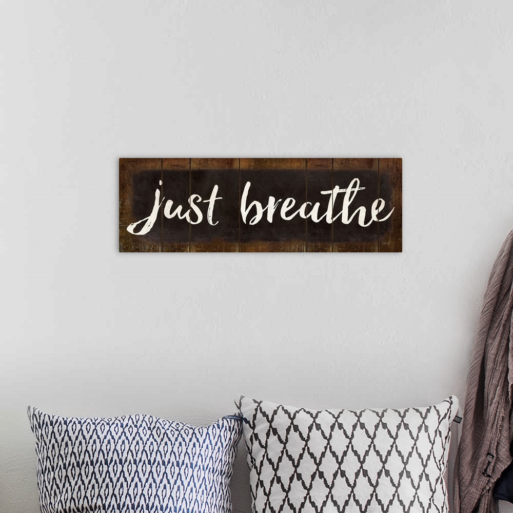 A bohemian room featuring "Just Breathe" in white handlettered script on a weathered brown background.