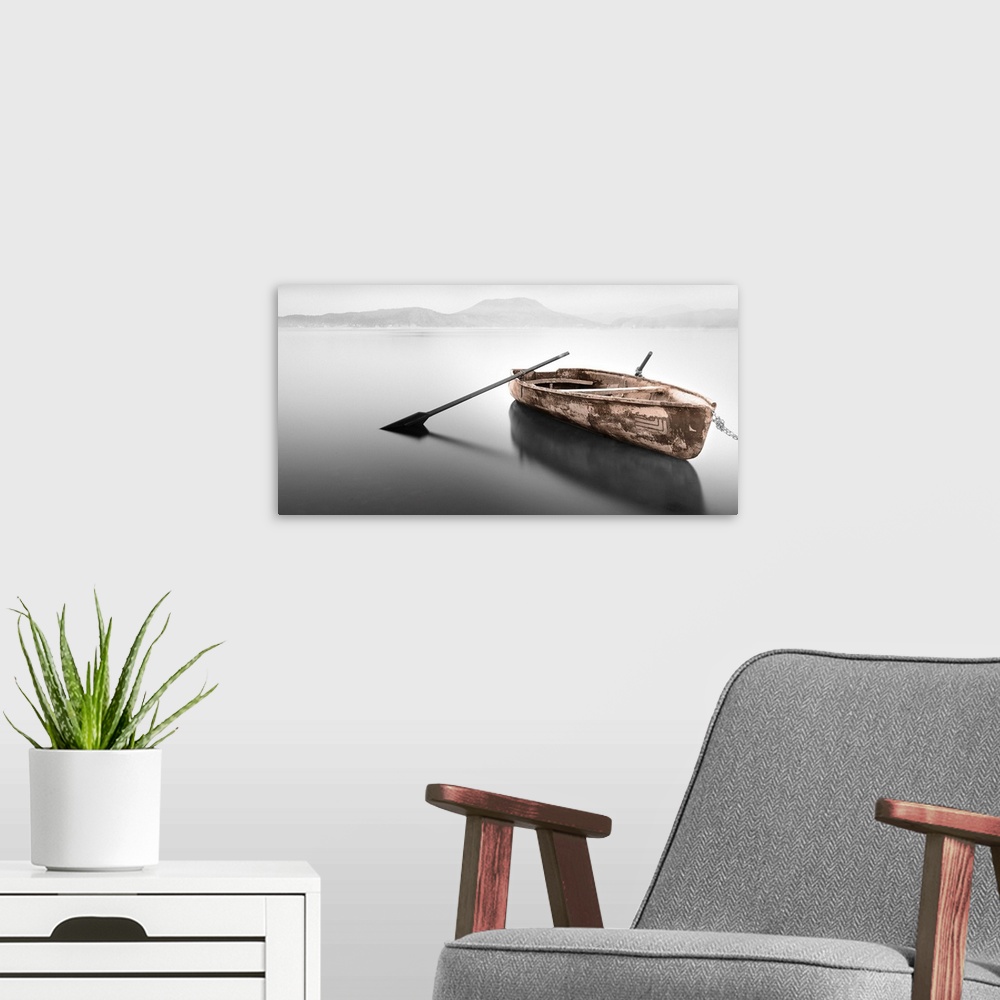 A modern room featuring An artistic photograph of a rowboat with no passenger sitting on flat water with a mountainous la...