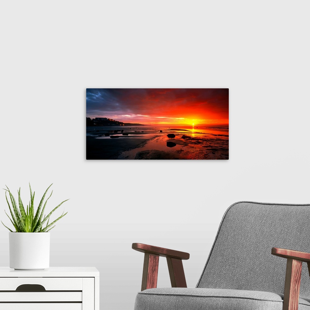 A modern room featuring Panoramic photograph that captures a colorful sunset on the shores of England.  The calm beach is...