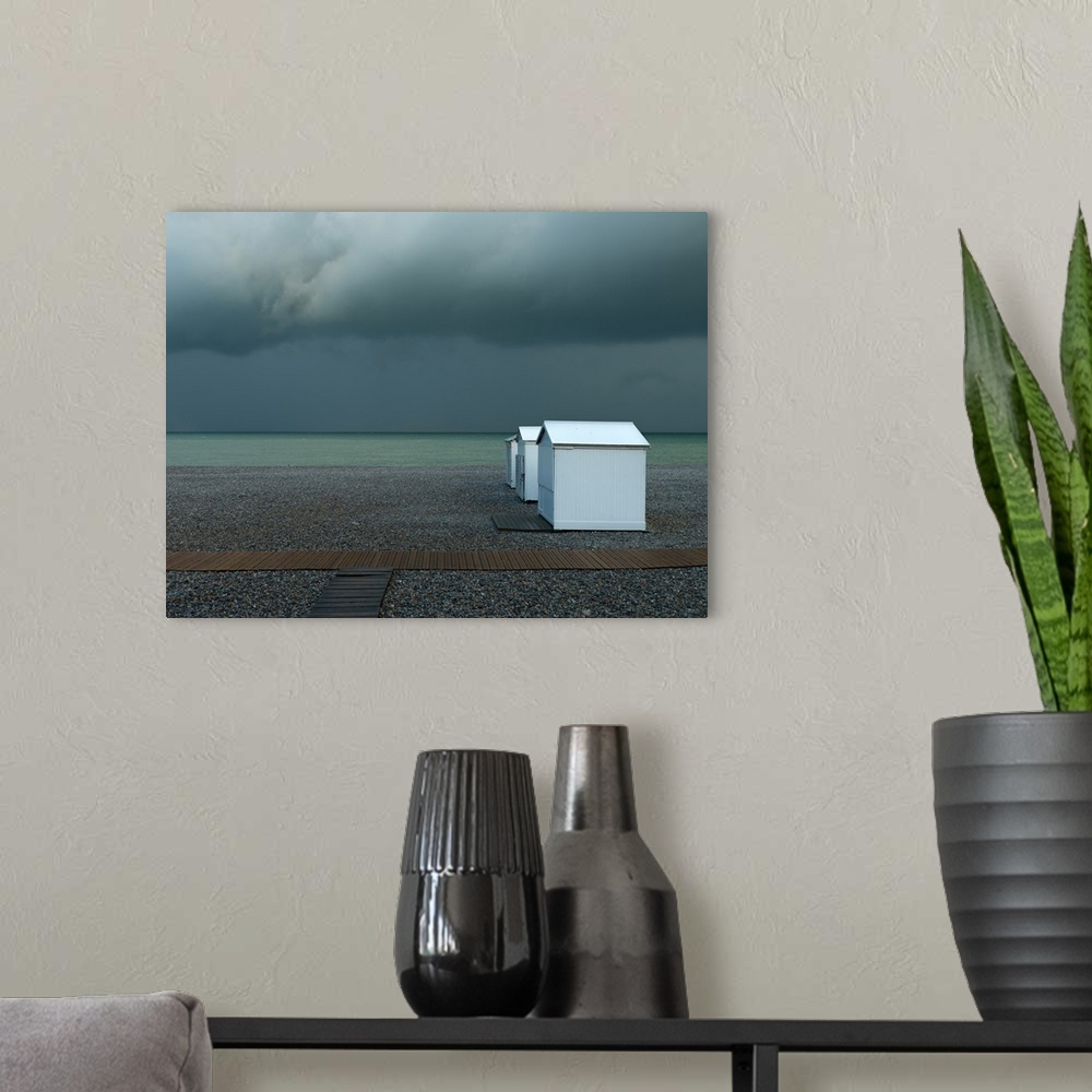 A modern room featuring Photograph of a pebble beach shore with a row of white beach cottages on an overcast day.
