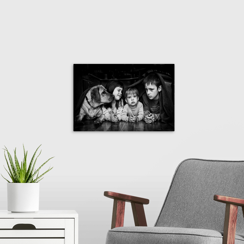 A modern room featuring Three siblings and their dog hiding together under a blanket.