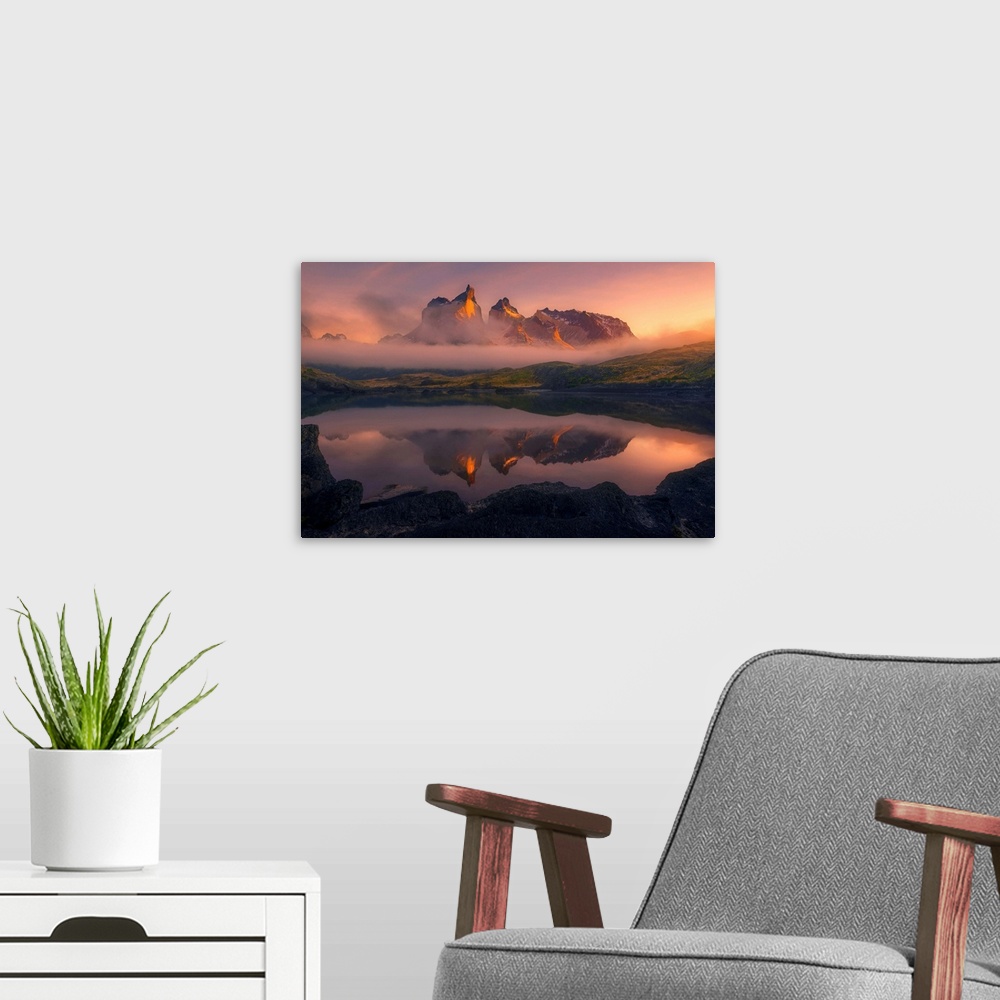 A modern room featuring Los Cuernos del Paine peaks through low clouds illuminated by the rising sun on a foggy morning.