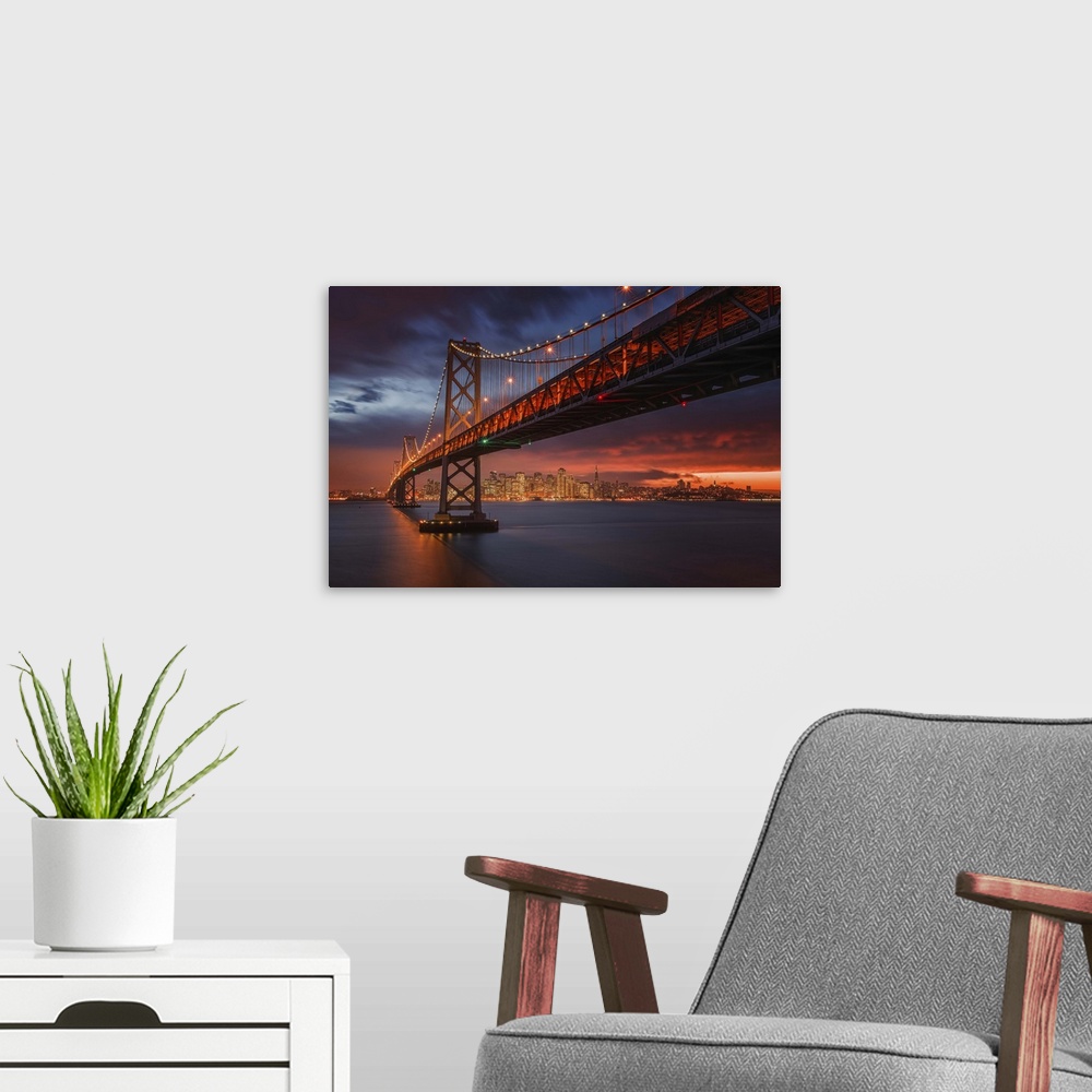A modern room featuring The San Francisco bay bridge illuminated at night with a glowing sunset sky hanging over the city...