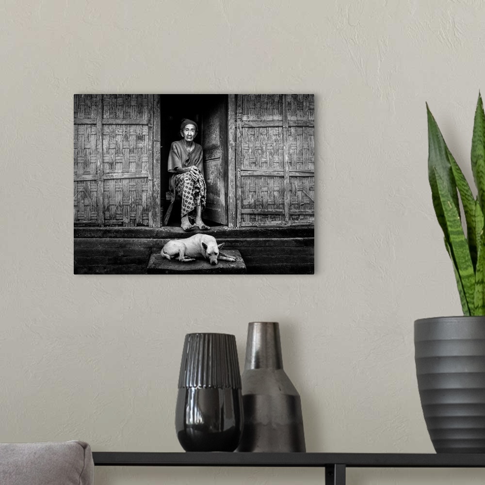A modern room featuring An elderly woman sitting in her doorway with a dog at her feet, Bangli, Bali, Indonesia.
