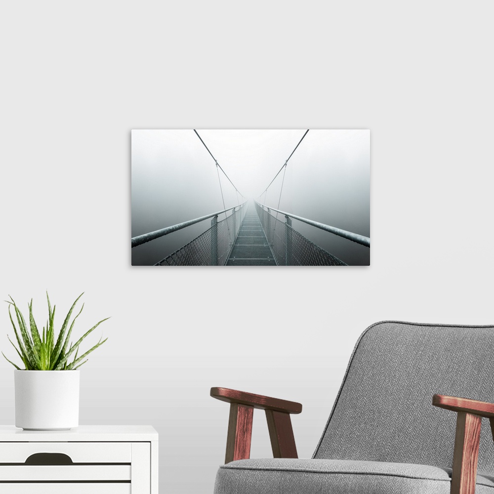A modern room featuring Vanishing point view of the walkway and cables of a bridge, disappearing into the fog.